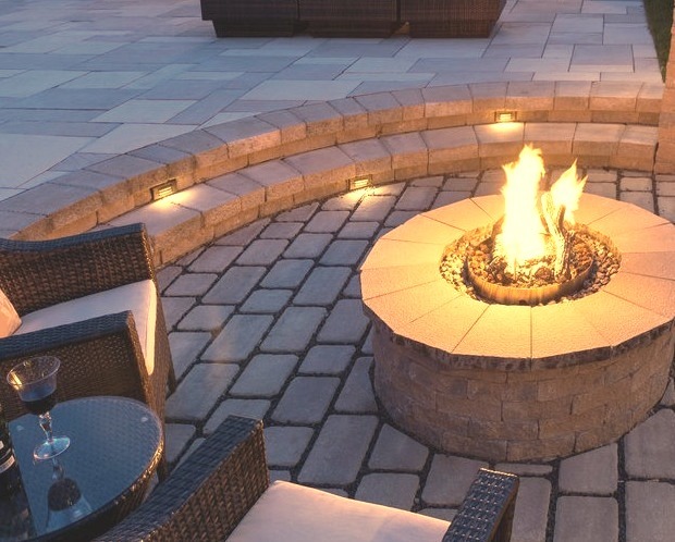 An expansive image of a transitional backyard stone patio with a fire pit
